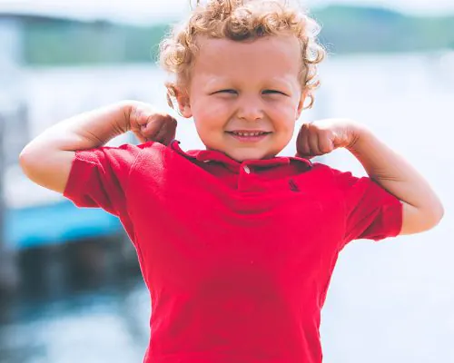 Young child in a red shirt flexing their arms